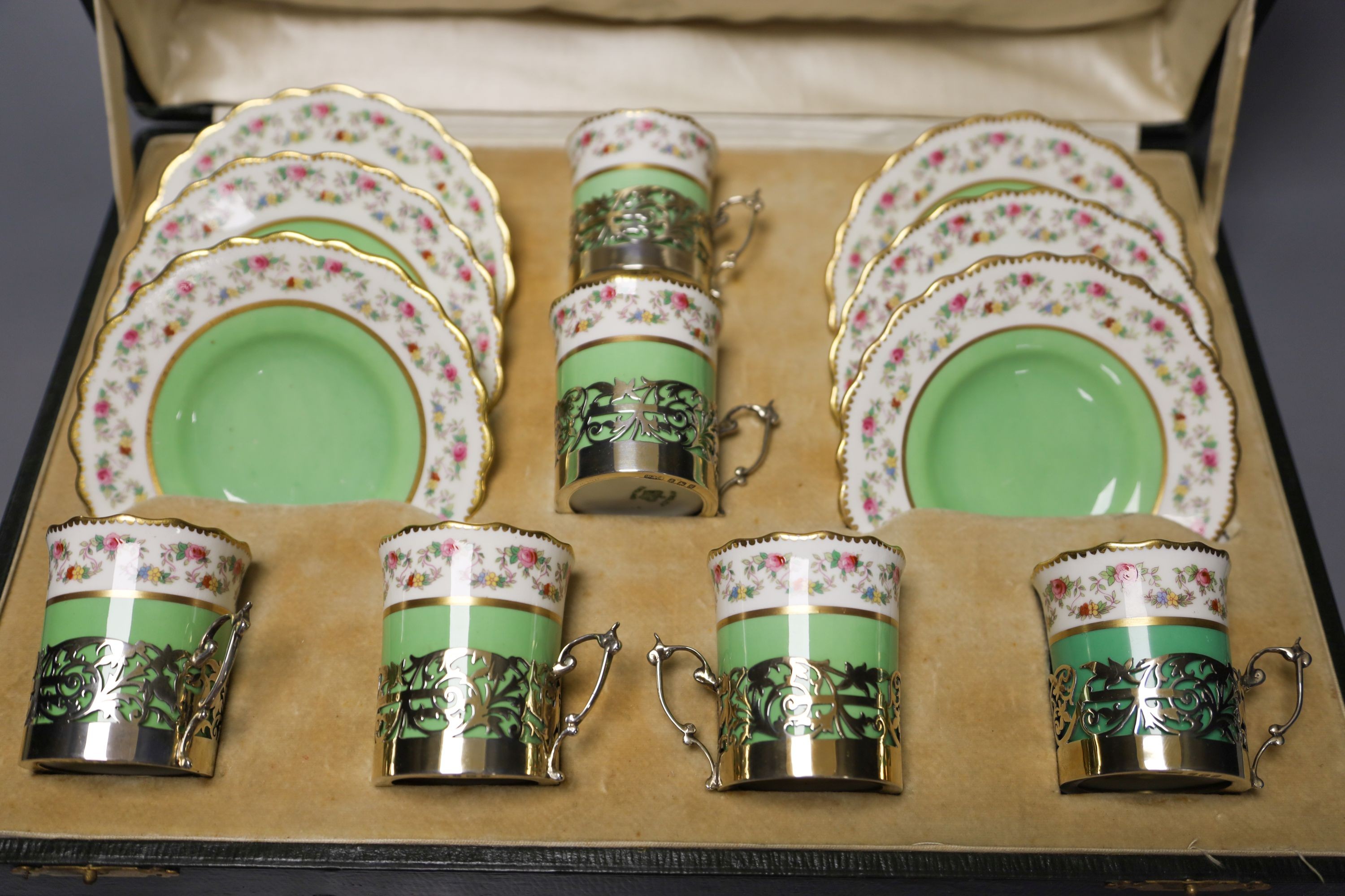 A set of six Aynsley coffee cans and saucers, with silver holders and a set of six silver spoons